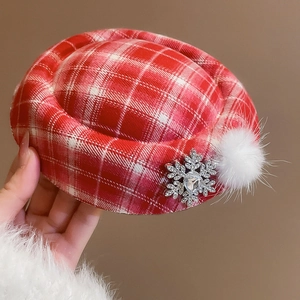 Detailed view of red plaid beret clip with white faux fur pompom and snowflake brooch