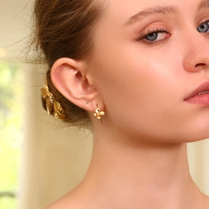 Detailed view of 18K gold plated four-petal flower dangle earring on a model