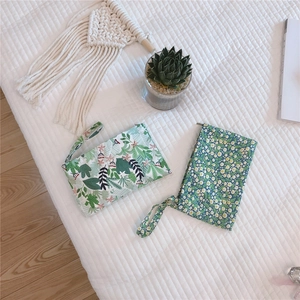 Floral cotton mini pouches with wristlets and metal zippers on a white textured surface