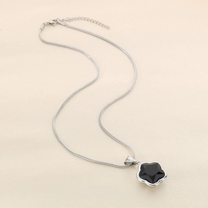 Detail of silver snake chain with a black five-petal flower pendant on beige surface