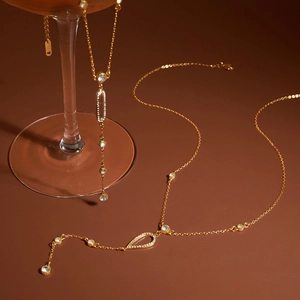 Macro shot of gold Y-shaped necklace with drop-shaped rhinestones on a wine glass
