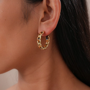 Détail macro d'une boucle d'oreille créole dorée avec texture cuir tressé marron sur un mannequin