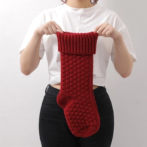 Classic red knitted Christmas stocking with square texture held by model for decor