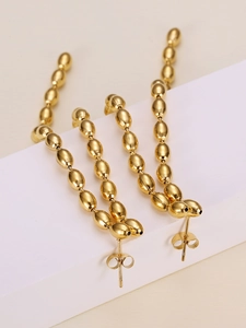 Detail of gold beaded drop earrings with polished oval charms on a white display block