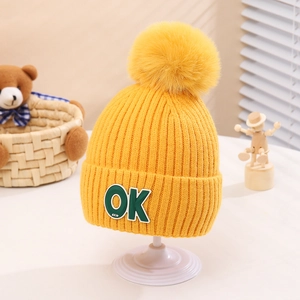 Detail of yellow knit beanie featuring a large pompom and a stitched OK logo patch
