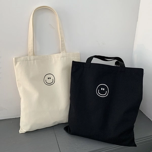 Minimalist canvas tote bags in cream and black featuring a simple linear smiley face design