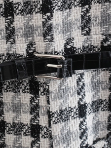 Vista macro del tessuto in tweed bianco e nero con cintura a coccodrillo e fibbia argento