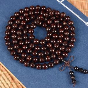 Polished red sandalwood prayer beads with golden star grains and a silk tassel on bamboo