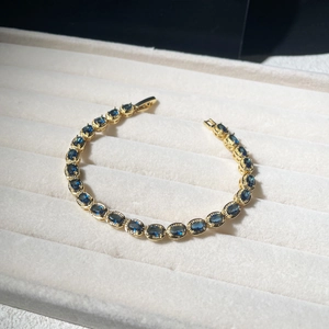 Detail of gold bracelet with oval blue gemstones and beaded metal texture on tray