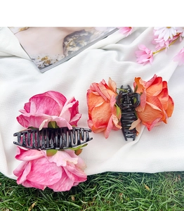 Close-up of pink and orange floral hair claws on white fabric with a natural grass backdrop