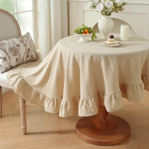 Close-up of beige round cotton linen tablecloth with pleated ruffle edge on dining table