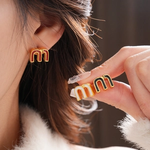 Close-up of stylish M-shaped enamel stud earrings in red, black, and white colors