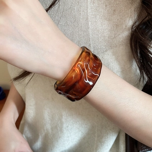 Detailed close-up of amber acrylic cuff bracelet with stylish wavy texture on a model