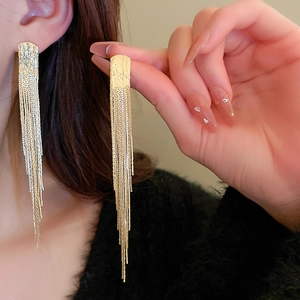 Macro detail of golden geometric chain tassel earrings on model with high gloss finish
