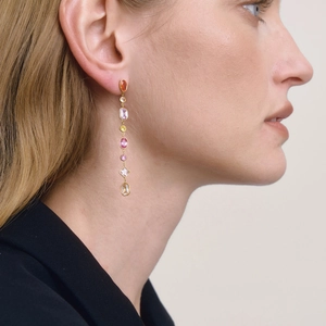 Detailed view of long gold drop earrings with seven colorful faceted gemstones on model