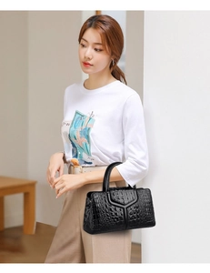 Detail of a black faux crocodile leather handbag held by a model with a V-shaped flap