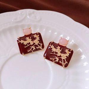Detail of vintage enamel earrings with red floral relief on white ceramic plate