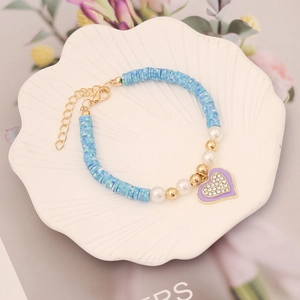 Detail of blue clay bead bracelet with heart pendant and pearls in a ceramic dish