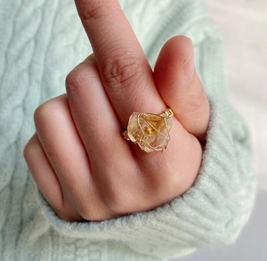 Detail of handcrafted wire-wrapped raw citrine ring with gold wire on a model's finger