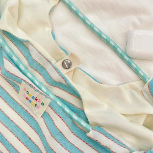 Close-up of blue striped canvas bag with green woven handle and metal snap button