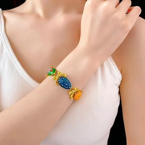 Dettaglio di un bracciale dorato vintage con ciondoli in smalto colorato al polso