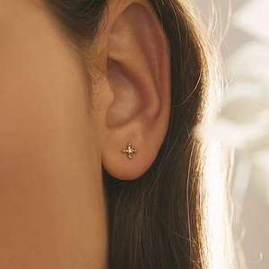 Close-up of a 16G gold cross cartilage stud with a small diamond worn by a model