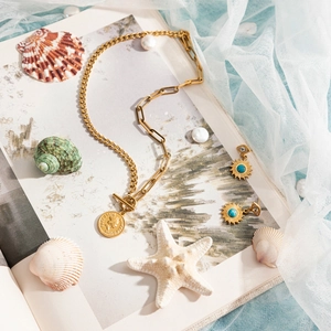 Detail of gold coin necklace and sun earrings with turquoise on shells and tulle