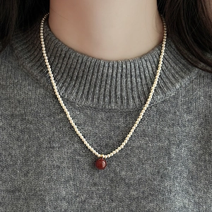 Close-up of pearl bead necklace with a round reddish-brown gemstone on a grey sweater