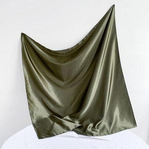 Close-up of dark green satin silk scarf draped on a table with soft shadows
