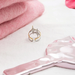 Close-up of a two-tone star-shaped ring in gold and silver on a soft pink background