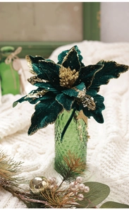 Detail of green velvet Christmas flower with gold sequins in a green glass vase
