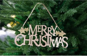 Detail of wooden Merry Christmas sign with gold glitter stars hanging on a green tree