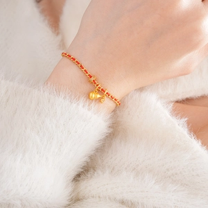 Gros plan d'un bracelet tressé rouge avec breloque gourde dorée et détails en zircon