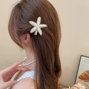 Détail d'une barrette étoile de mer tressée avec strass portée sur le côté des cheveux