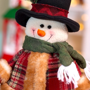 Close-up of a festive snowman plush with a green knit scarf and a red plaid hat