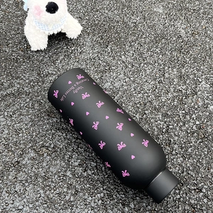 Détail d'un flacon isotherme noir mat avec motif nœud rose sur fond d'asphalte