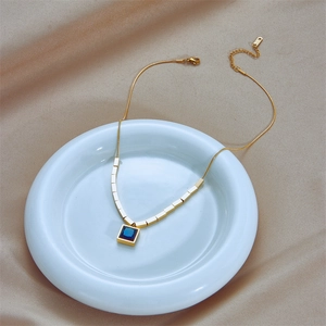 Minimalist gold necklace with square blue gemstone pendant on elegant silk background