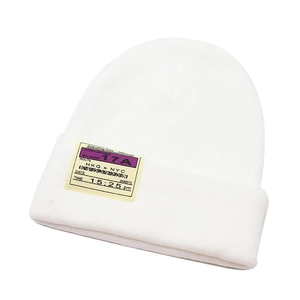 Detail of white knit beanie featuring yellow boarding pass style embroidery patch