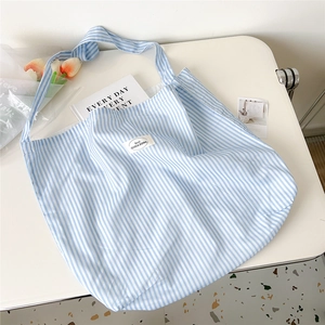 Detail of blue and white striped canvas tote bag on a white table with fresh tulips
