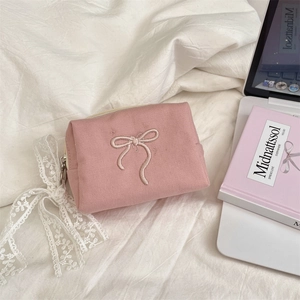 Detailed shot of pink canvas makeup bag with bow embroidery on a cozy white bedsheet