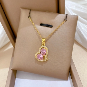 Close-up of heart-shaped pink gem pendant on gold chain necklace against white silk