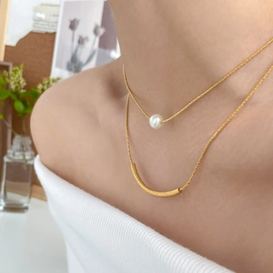 Close-up of a double-layered gold chain necklace with a pearl and frosted curved pendant