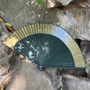 Classic dark green gradient Chinese folding fan with leaf patterns on a rock background