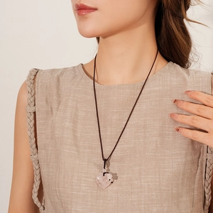 Close-up of pink quartz heart pendant on black braided rope necklace worn by a model