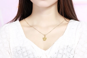 Primo piano della collana dorata con ali d'angelo e ciondolo lettera M su modella