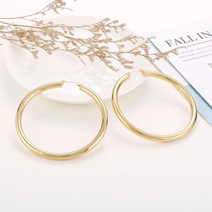 Detailed view of large polished 18K gold hoop earrings on a minimalist white backdrop