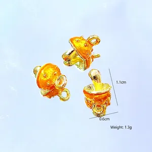 Macro detail of miniature mushroom charms with orange enamel finish and gold plating