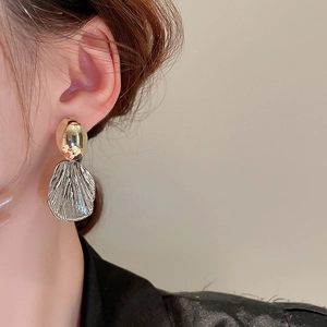 Detail of elegant two-tone gold and silver earrings on a model with shell texture