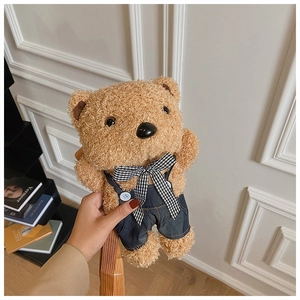 Close-up of brown plush teddy bear bag wearing blue denim overalls and checkered bowtie
