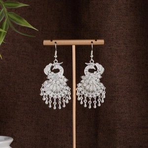 Detailed shot of silver peacock earrings with hollow carvings and teardrop tassels